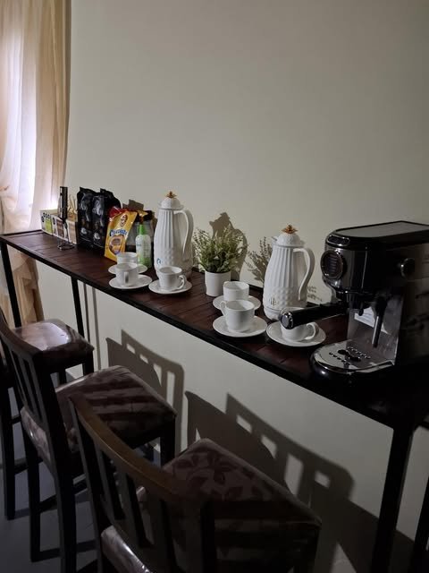 Barra de madera con cafetera, termos, tazas y banquetas altas en el rincón de café de Gym Brasil